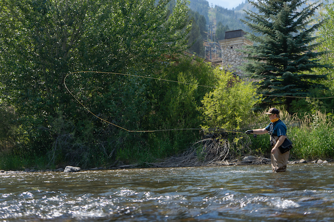 A person casts a fly rod in the river